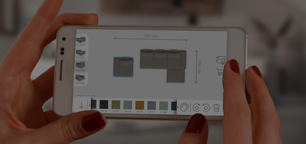 Eine Hand hält ein Smartphone mit dem FEYDOM Konfigurator, auf dem Bildschirm ein zusammengestelltes Sofa mit Maßen
